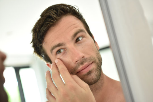 Handsome man applying facial cream in front of mirror