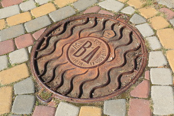 Rusted manhole on a street with pavement from multicolor block