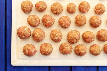 Raw homemade meatballs on white plastic cutting board overhead v
