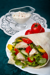 Shawarma on a white plate with a white sauce, doner kebab, traditional roll with meat and pita bread, selective focus on the filling