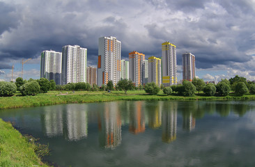 Fototapeta na wymiar Городской пейзаж новостроек в парке с водоёмом.