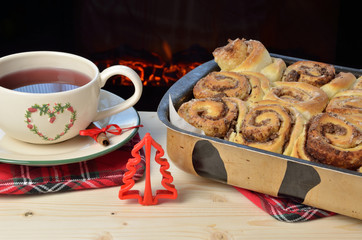 Pan with fresh cinnamon rolls with tea by the fireplace