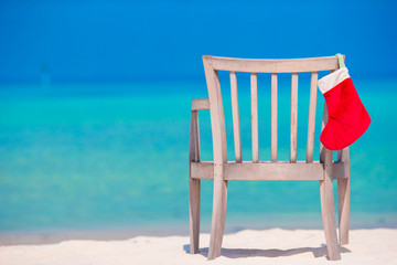 Red Christmas stocking at tropical white beach. Christmas concept
