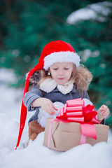 Adorable little girl with Christmas box gift in winter outdoors on Xmas eve