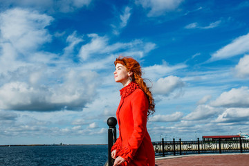 portrait of young redhead woman in red winter coat against the blue sky