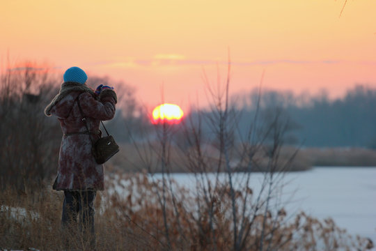 Woman taking picture of winter sunset