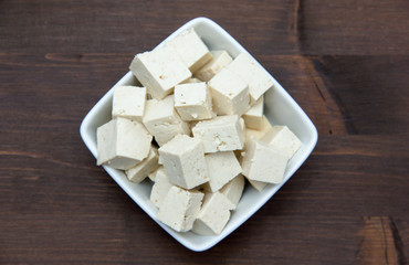 Cubes of tofu square bowl on wooden table seen from above