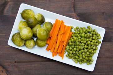 Tray with steamed vegetables on wooden table seen from above