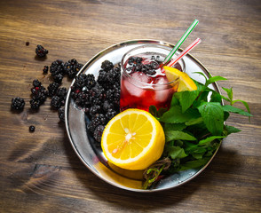 Berry cocktail in glass with ice, lemon and mint leaves on a wooden table .