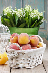 Basket of peaches on wooden table, bucket with lily of the valle