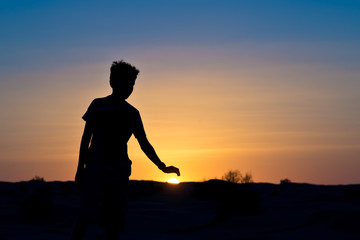 Silhouette of a boy covering the sun with his hand