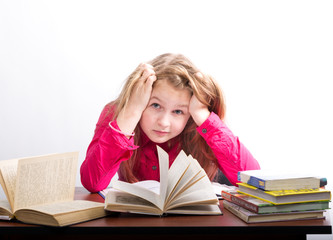 teenager girl sitting at a table in front of her large pile of books. schoolgirl reading a book and doing homework