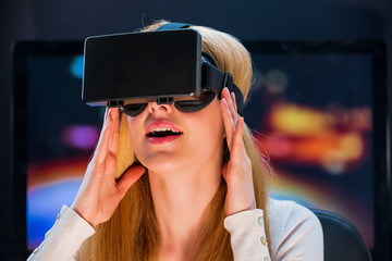 Blond girl with pleasure uses head-mounted display. Looking around in virtual reality. Lights on...