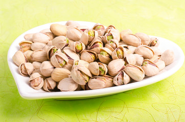 Salt pistachios on the white plate on green background.