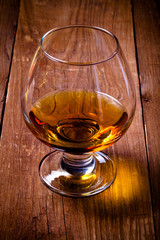 Cognac in a glass goblet on the old wooden table. Toned