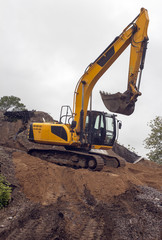 heavy yellow excavator with shovel standing on hill
