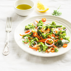 healthy salad with broccoli and carrots on a white plate on a light surface