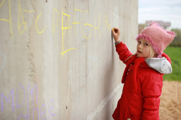 the girl in a red jacket thinks and writes with letter chalk on a wall