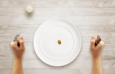 Diet concept of breakfast. Olive in an empty plate with hands on table.