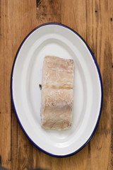 frozen cod fish on white plate on brown wooden background