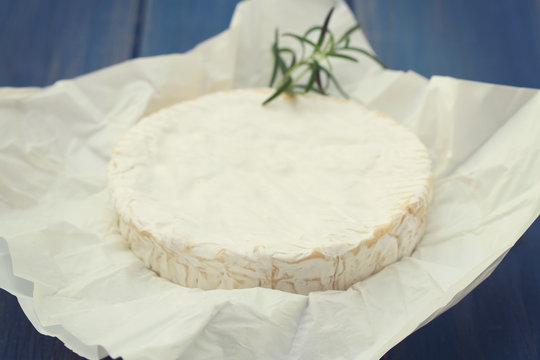 cheese with rosemary on white paper on blue wooden background