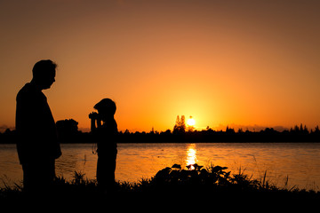 silhouette father and son play binoculars sunset background
