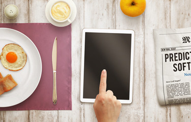 Hand uses a tablet during breakfast. Isolated screen display. Top view scene with food, coffee, apple, newspaper.