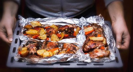 A man holding in his hands a pan with roasted rabbit and vegetables