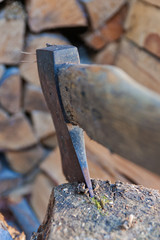 Close up of  old ax stuck in tree stump, woodpile on background