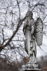Old tombstone sculpture of an angel with broken arm and wings on the cemetery.