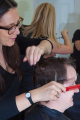 Female stylist sits combs a male client's hair in salon