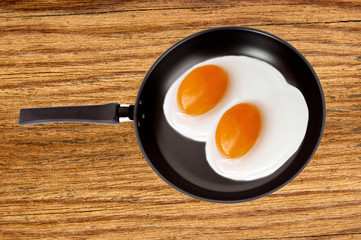 Two fried eggs on a pan on wooden table background