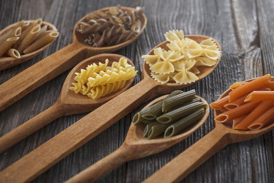 A set of raw pastas on spoons on a wooden table