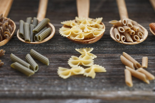A set of raw pastas on spoons on a wooden table