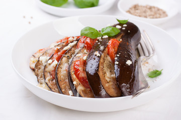 Baked eggplant with tomatoes, cheese and italian herbs on a white plate. closeup.