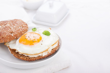 Bun with egg, cottage cheese and fresh basil on a white plate for breakfast. selective focus, horizontal.