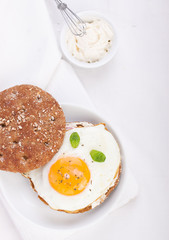 Bun with egg, cottage cheese and fresh basil on a white plate for breakfast. top view.