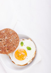 Bun with egg, cottage cheese and fresh basil on a white plate for breakfast. top view.