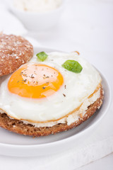 Bun with egg, cottage cheese and fresh basil on a white plate for breakfast. closeup