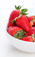 .Ripe red strawberries in a white ceramic bowl on a white background, closeup, selective focus.