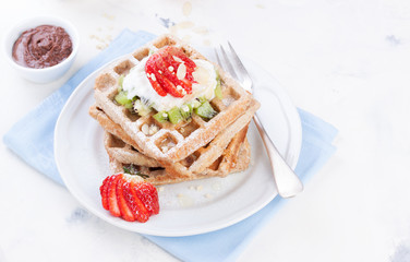 Waffles with wholewheat flour and fruits on a white plate on a blue napkin..