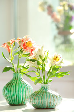 Beautiful Alstroemeria flowers in aquamarine vases on window background