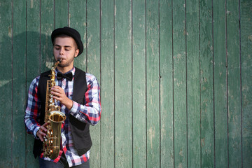 Handsome man plays saxophone on green wooden background