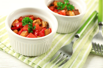 Tasty vegetarian ratatouille made of eggplants, squash, tomatoes in bowls on wooden table background