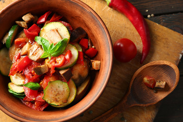 Tasty vegetarian ratatouille made of eggplants, squash, tomatoes in bowl on wooden table background