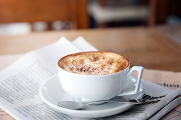 Cup of tasty cappuccino and newspapers on table