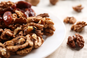 Walnut and date fruit in plate on wooden table, close-up