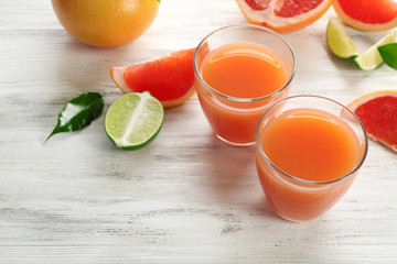 Two glasses of citrus juice and fresh fruits on light wooden background