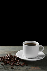 Cup of coffee and coffee grains on wooden table, on gray background