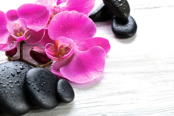 Beautiful composition of orchid and pebbles on white wooden background, close up